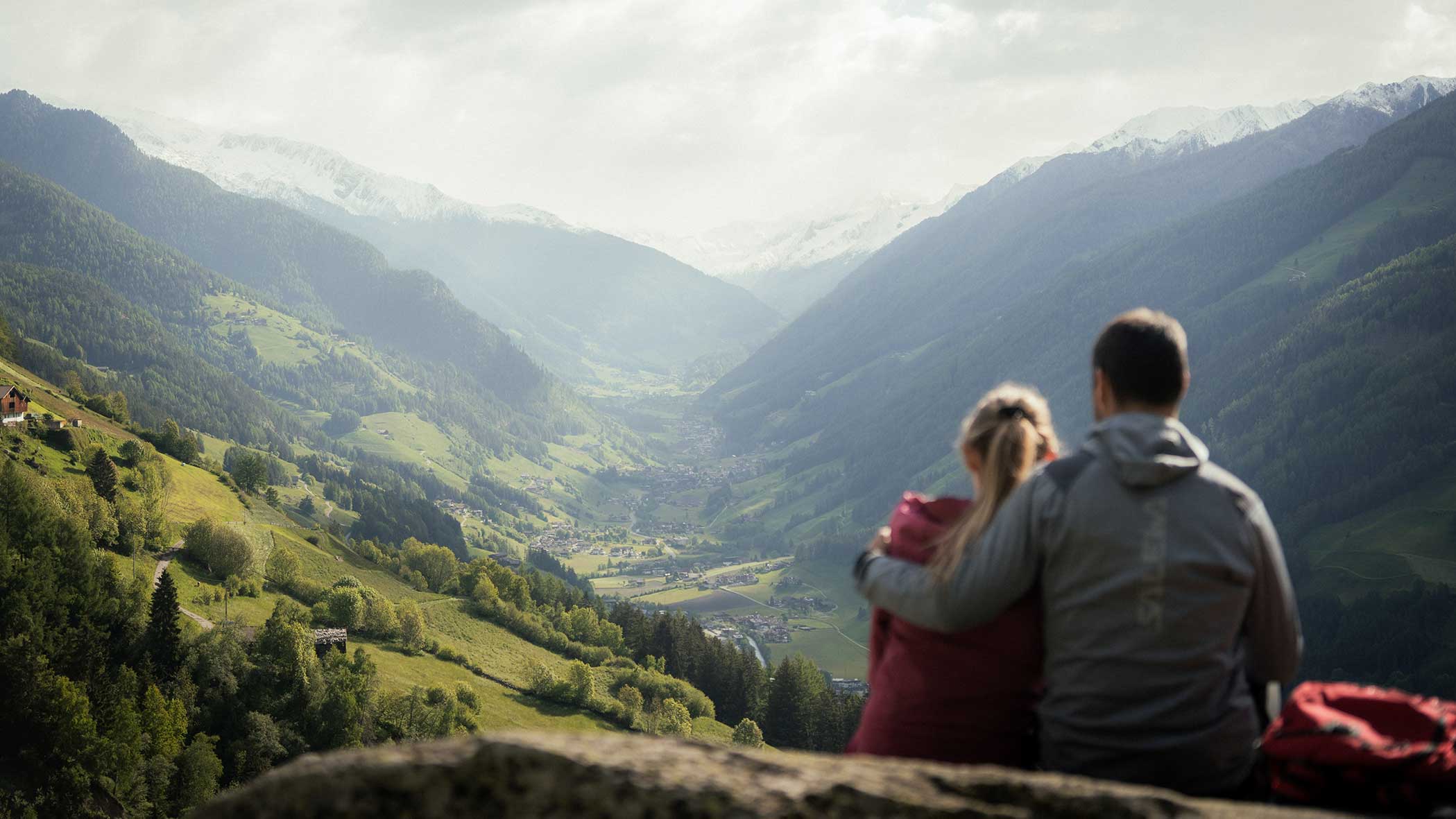 Ein Paar sitzt auf einem Felsen und blickt auf ein malerisches grünes Tal, das von Bergen umgeben ist. - Apartments & Chalet Selm