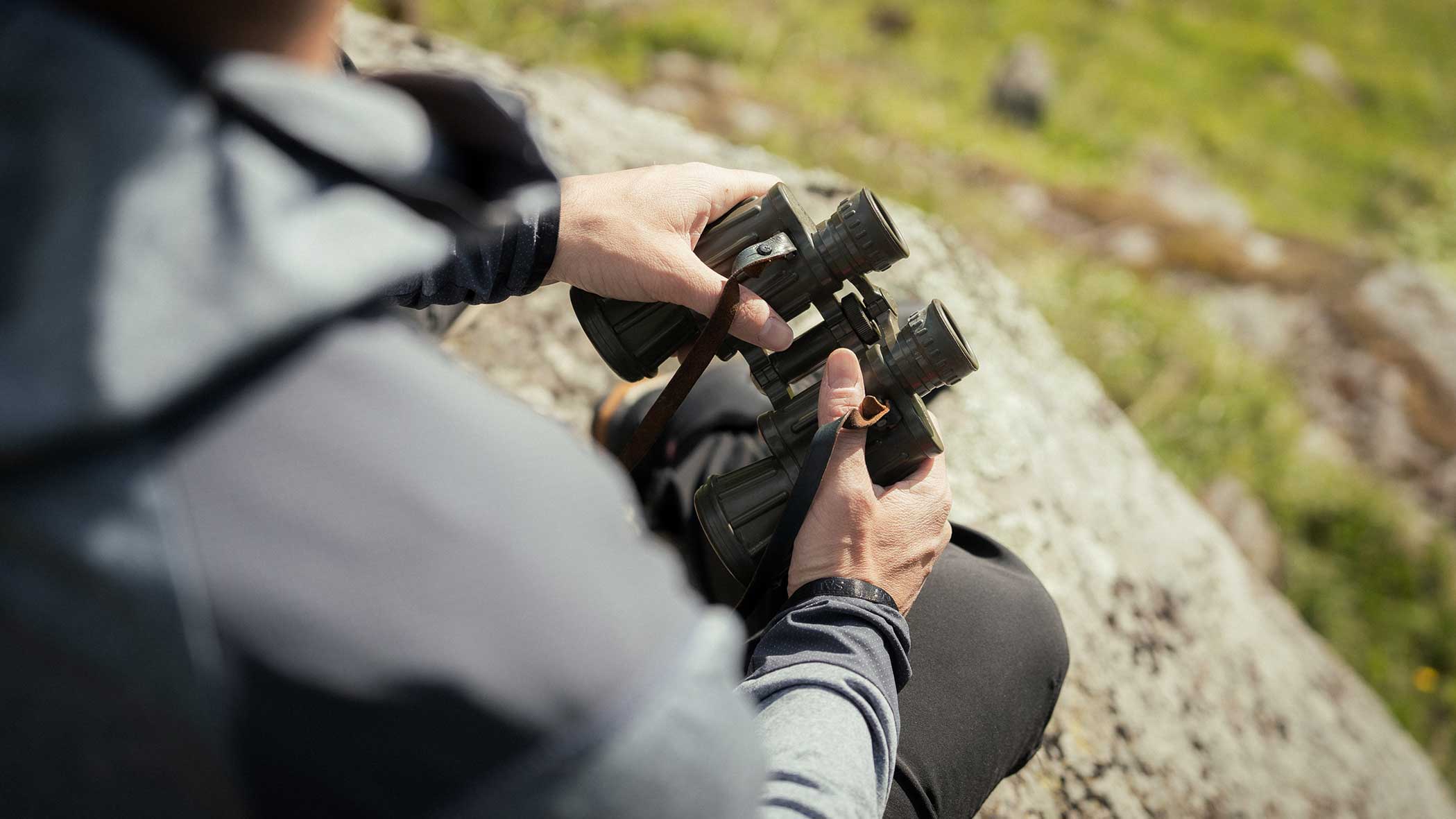 Person, die im Freien sitzt und ein Fernglas hält, mit Gras und Felsen im Hintergrund. - Apartments & Chalet Selm