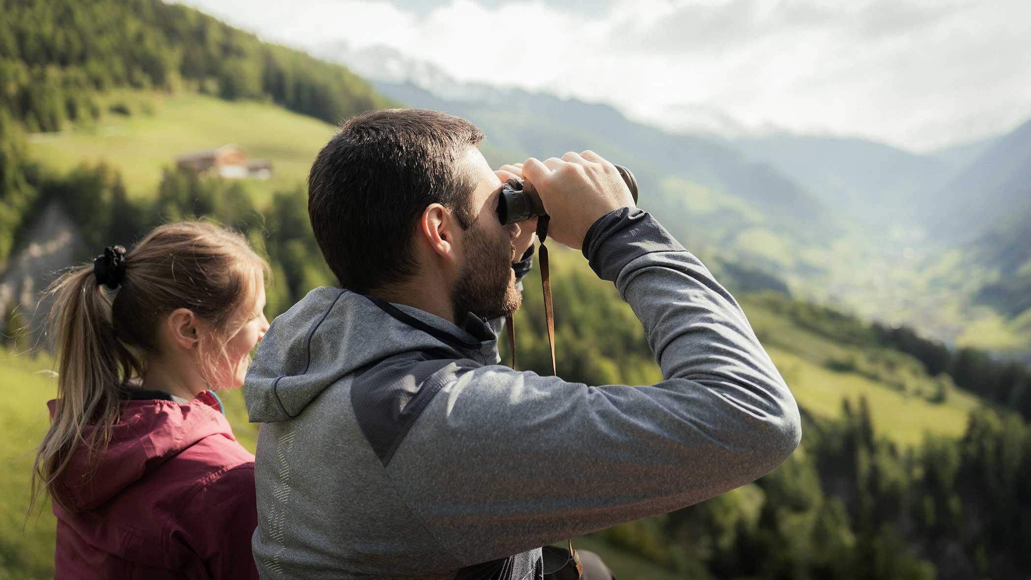 Zwei Personen betrachten im Freien ein malerisches Tal; einer benutzt ein Fernglas, während der andere daneben steht. - Apartments & Chalet Selm