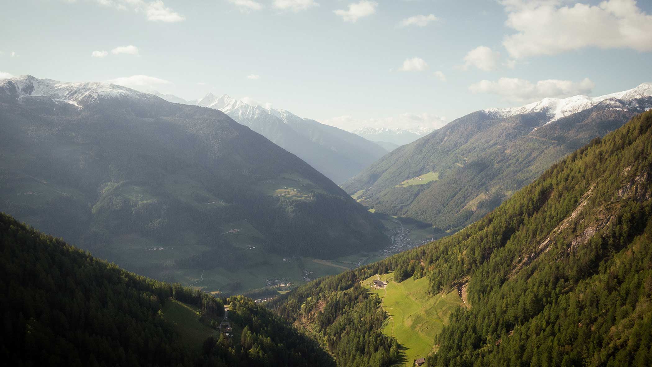 Gebirgstal mit grünen Hügeln, Wäldern und entfernten schneebedeckten Gipfeln unter einem teilweise bewölkten Himmel. - Apartments & Chalet Selm