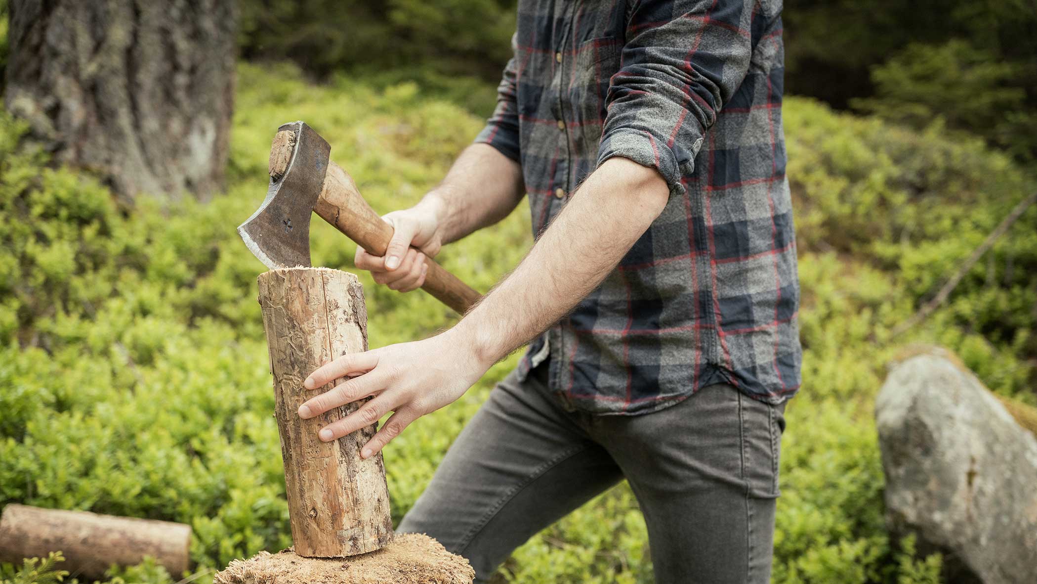 Eine Person in einem karierten Hemd spaltet einen Baumstamm mit einer Axt im Freien in einem Waldgebiet. - Apartments & Chalet Selm