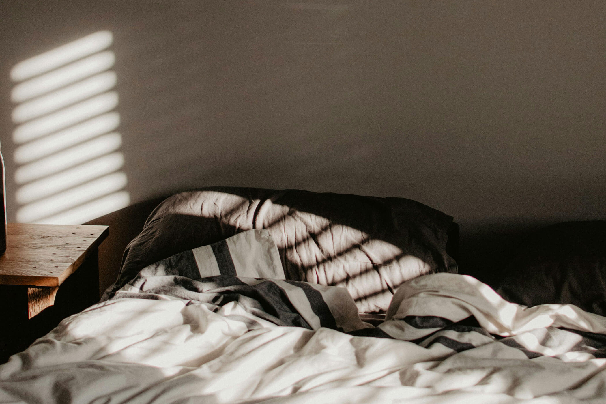 Ungemachtes Bett mit gestreifter Bettwäsche und Sonnenlicht, das durch die Jalousien fällt und Schatten auf das Bett wirft. - Apartments & Chalet Selm